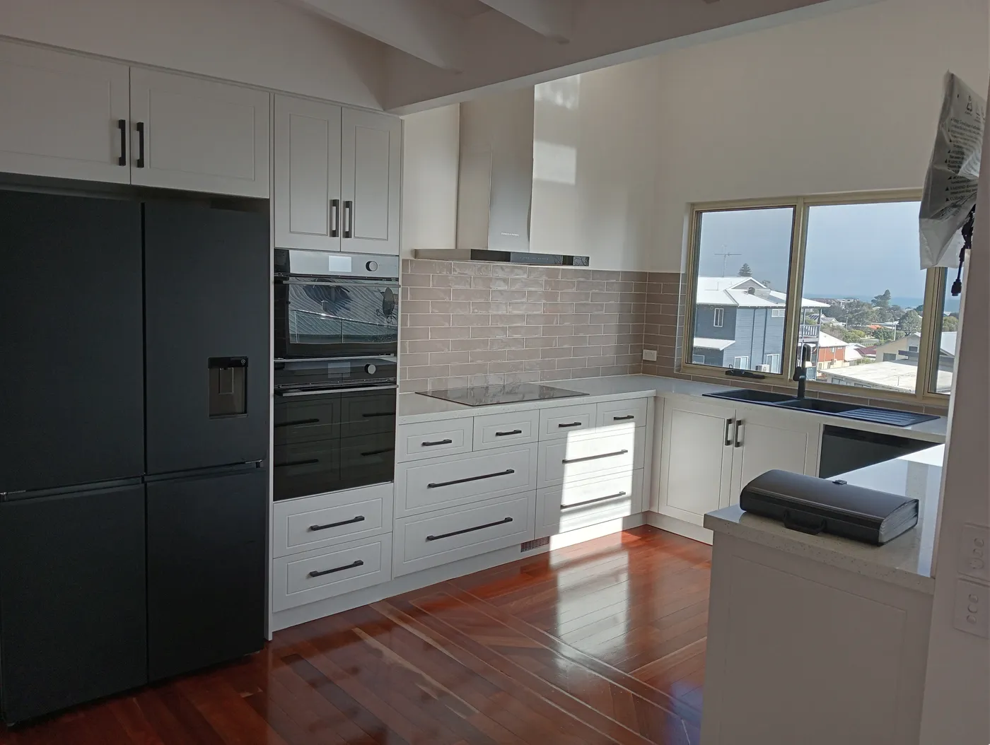 Renovated kitchen with white shaker cabinetry, stone benchtops and an ocean-view window